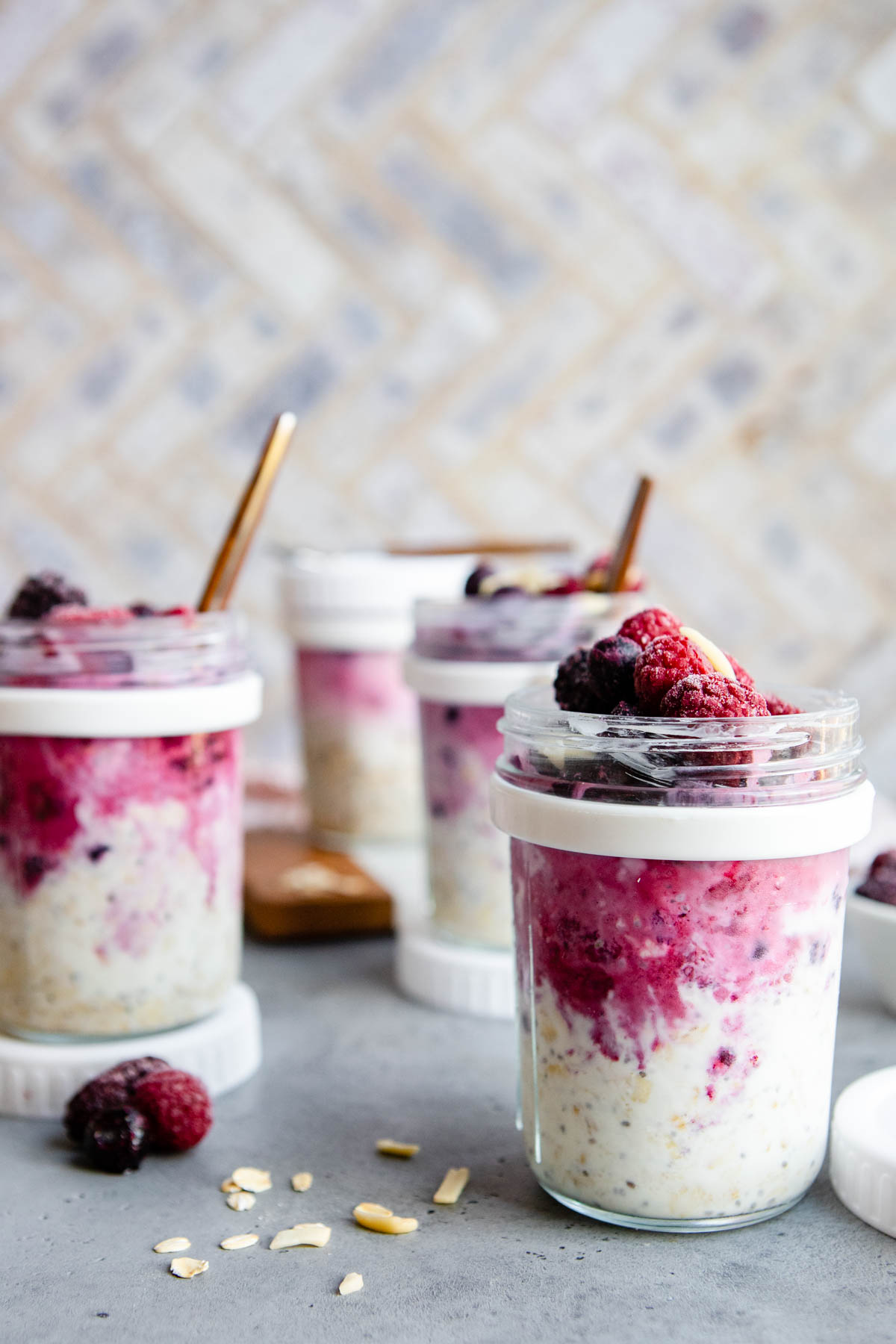 overnight oats with frozen fruit in meal prep jars on a gray surface 