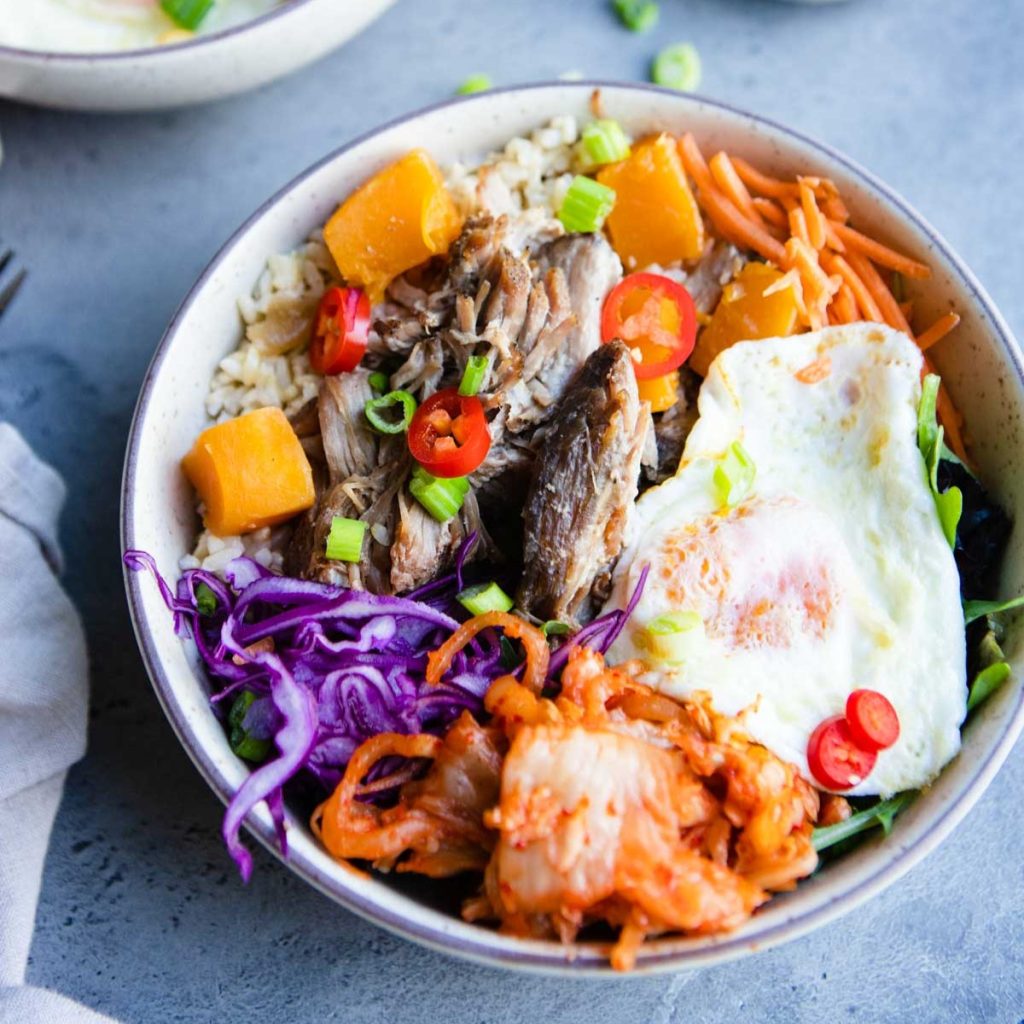 bowl filled with slow cooker pork and butternut squash, topped with an over easy egg and kimchi