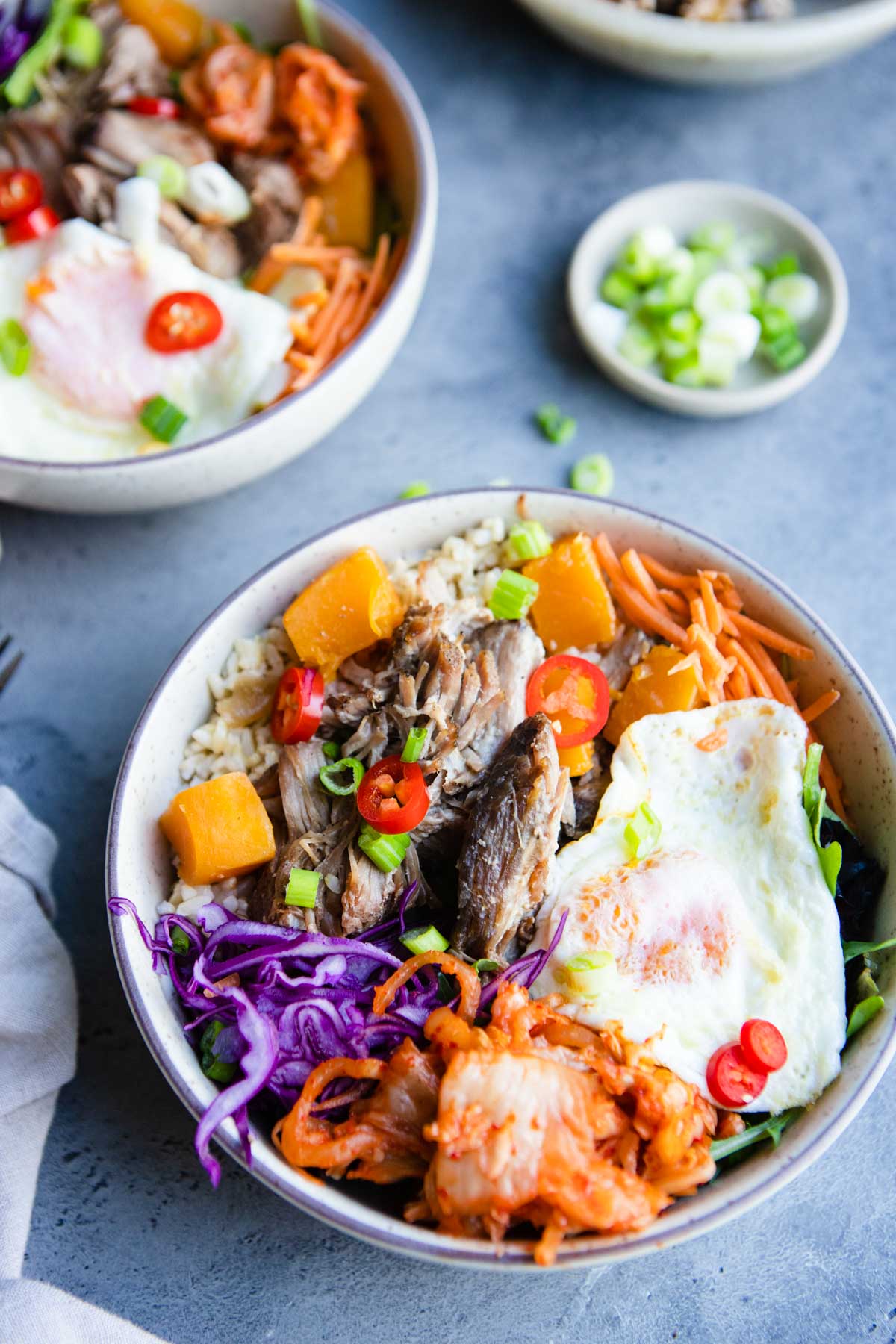 2 beige bowls filled with shredded pork, butternut squash and topped with veggie garnishes 