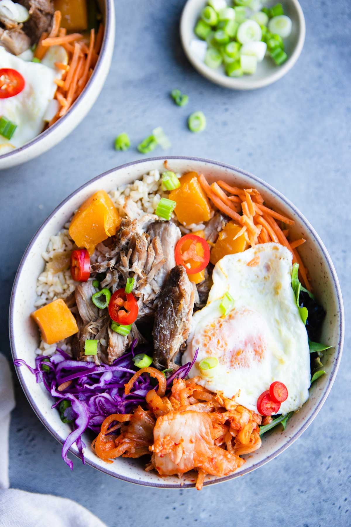 pork and squash served in a bowl topped with kimchi and over easy egg