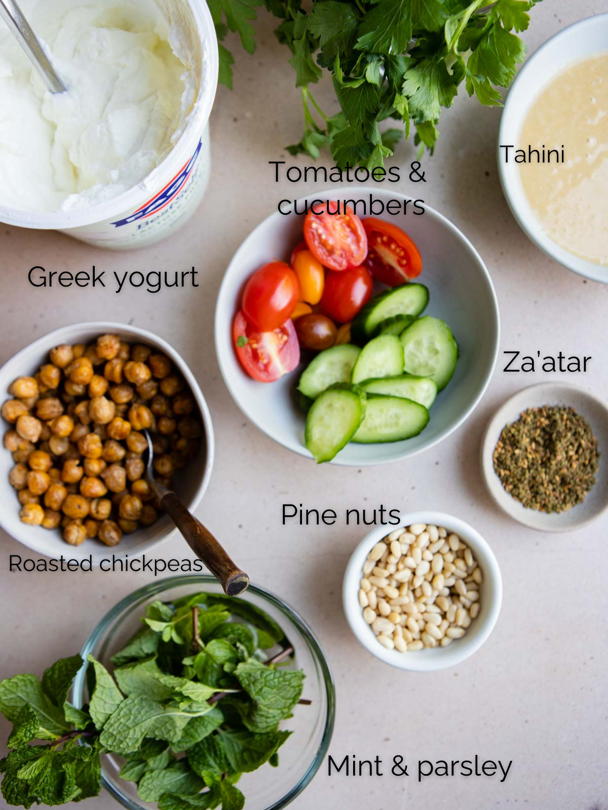 small white bowls filled with chopped tomatoes, zucchini, pine nuts, herbs, roasted chickpeas and Greek yogurt