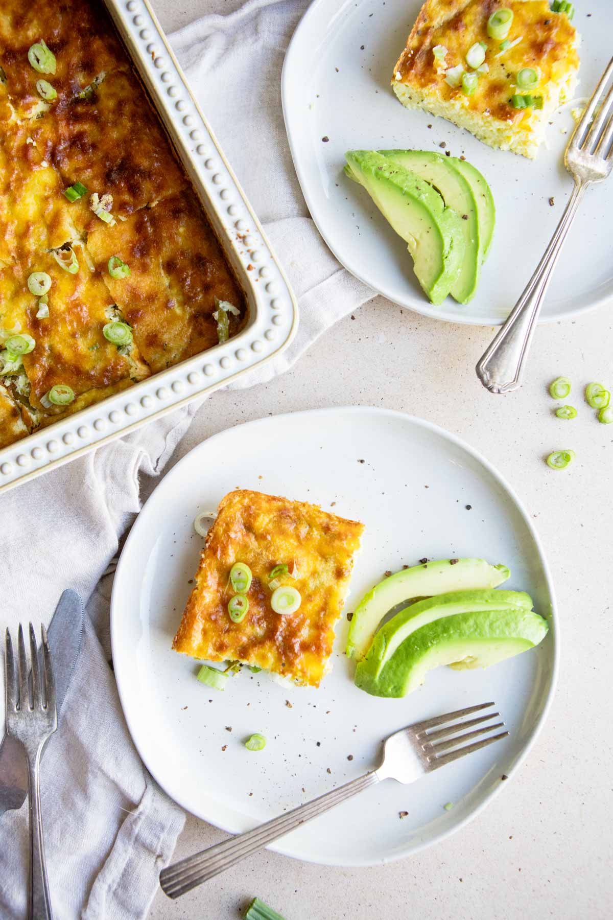 a piece of baked eggs and asparagus casserole on a white plate next to a casserole dish with baked eggs and asparagus 