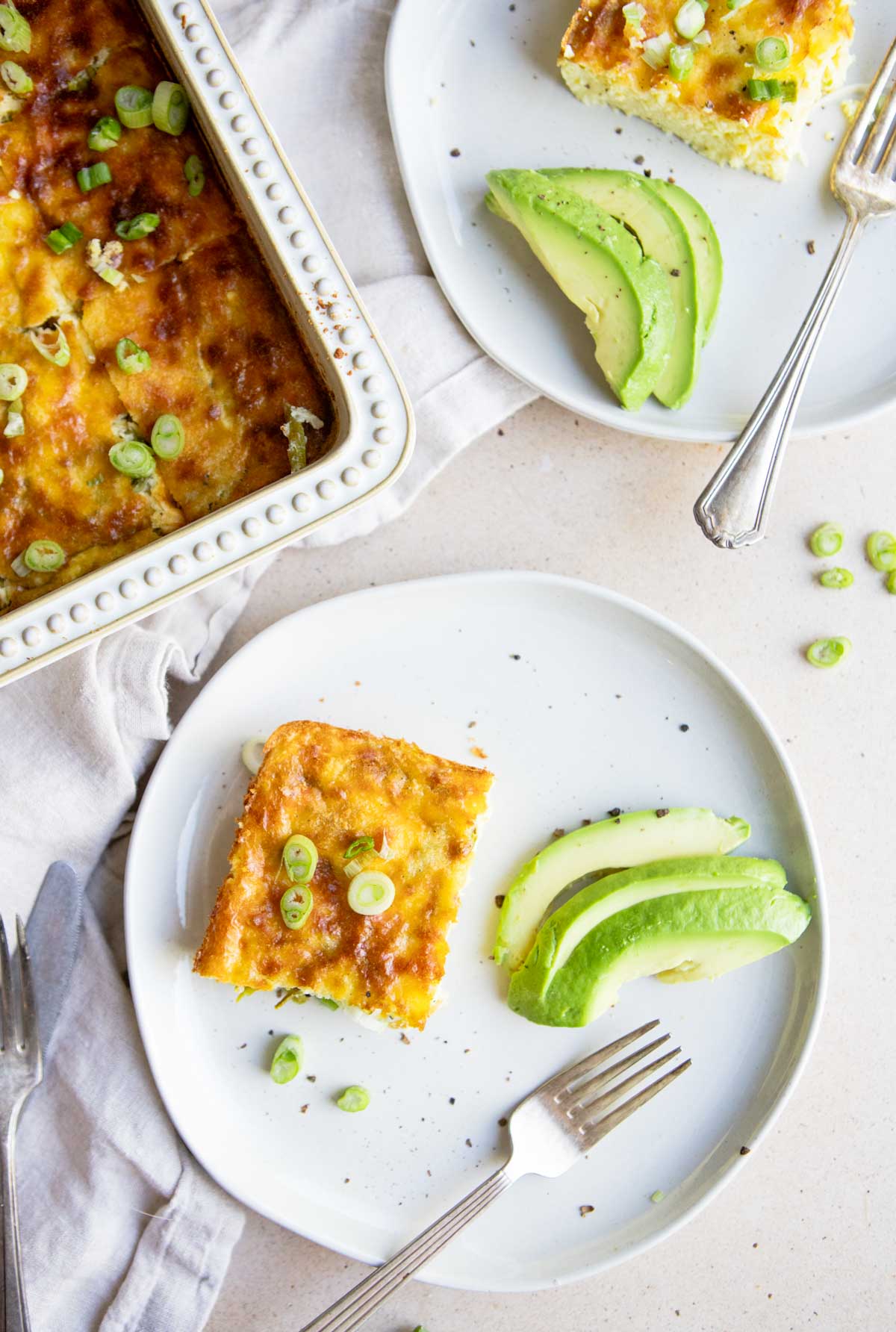 2 white round plates with pieces of eggs and asparagus casserole and sliced avocado 