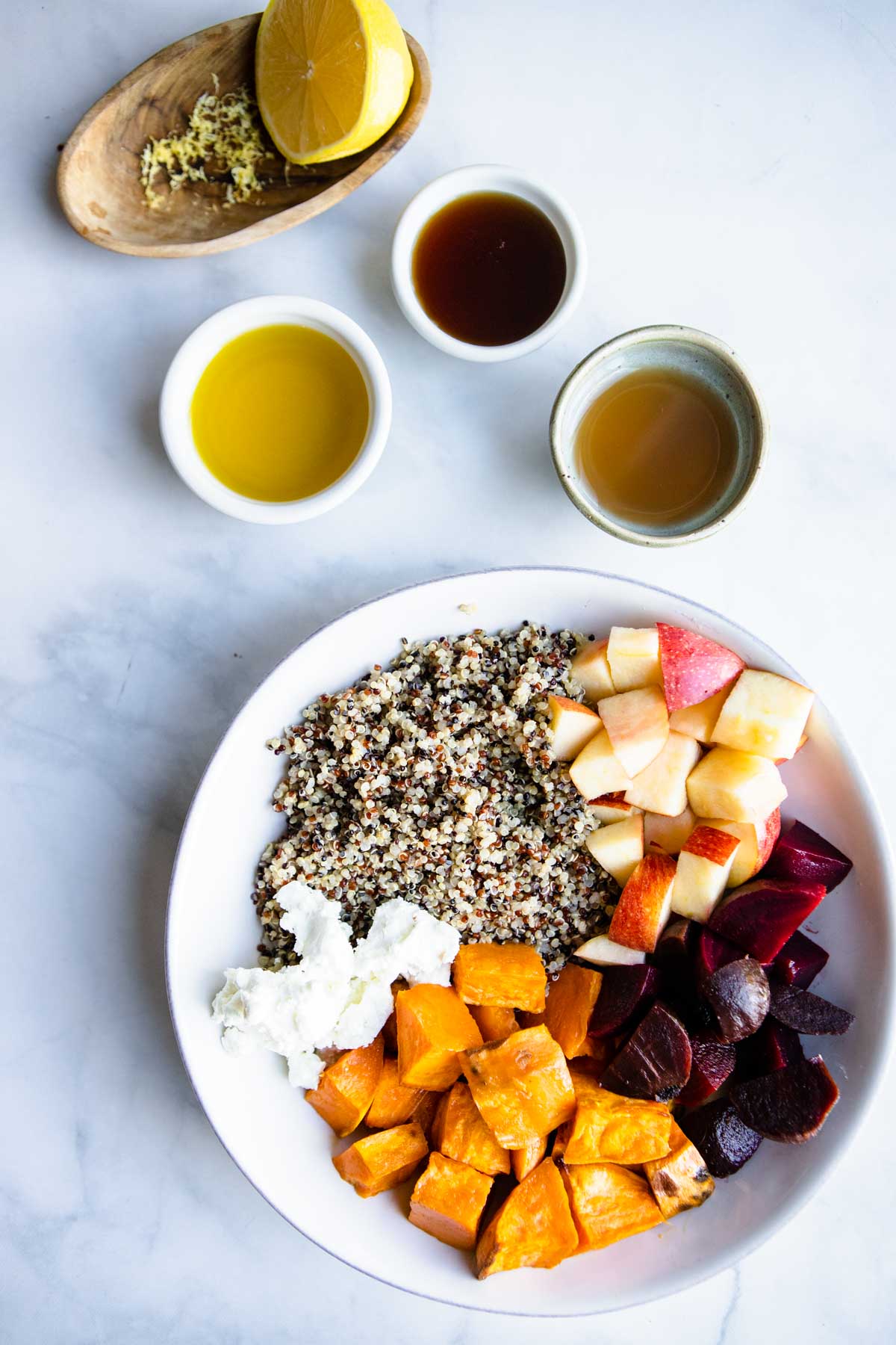 a bowl filled with cooked quinoa, roasted beets and sweet potatoes, diced apples and goat cheese. 