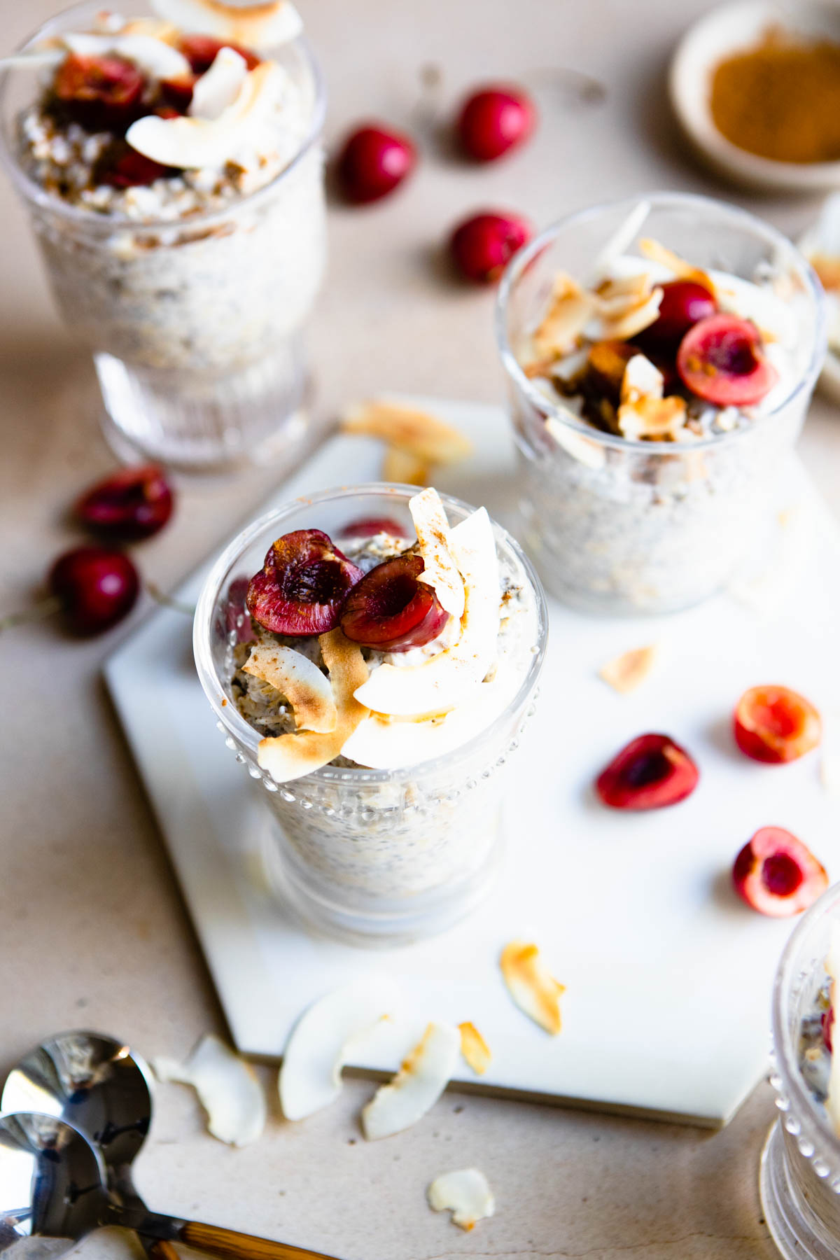 overnight oats in glass cups garnished with cherries and coconut flakes