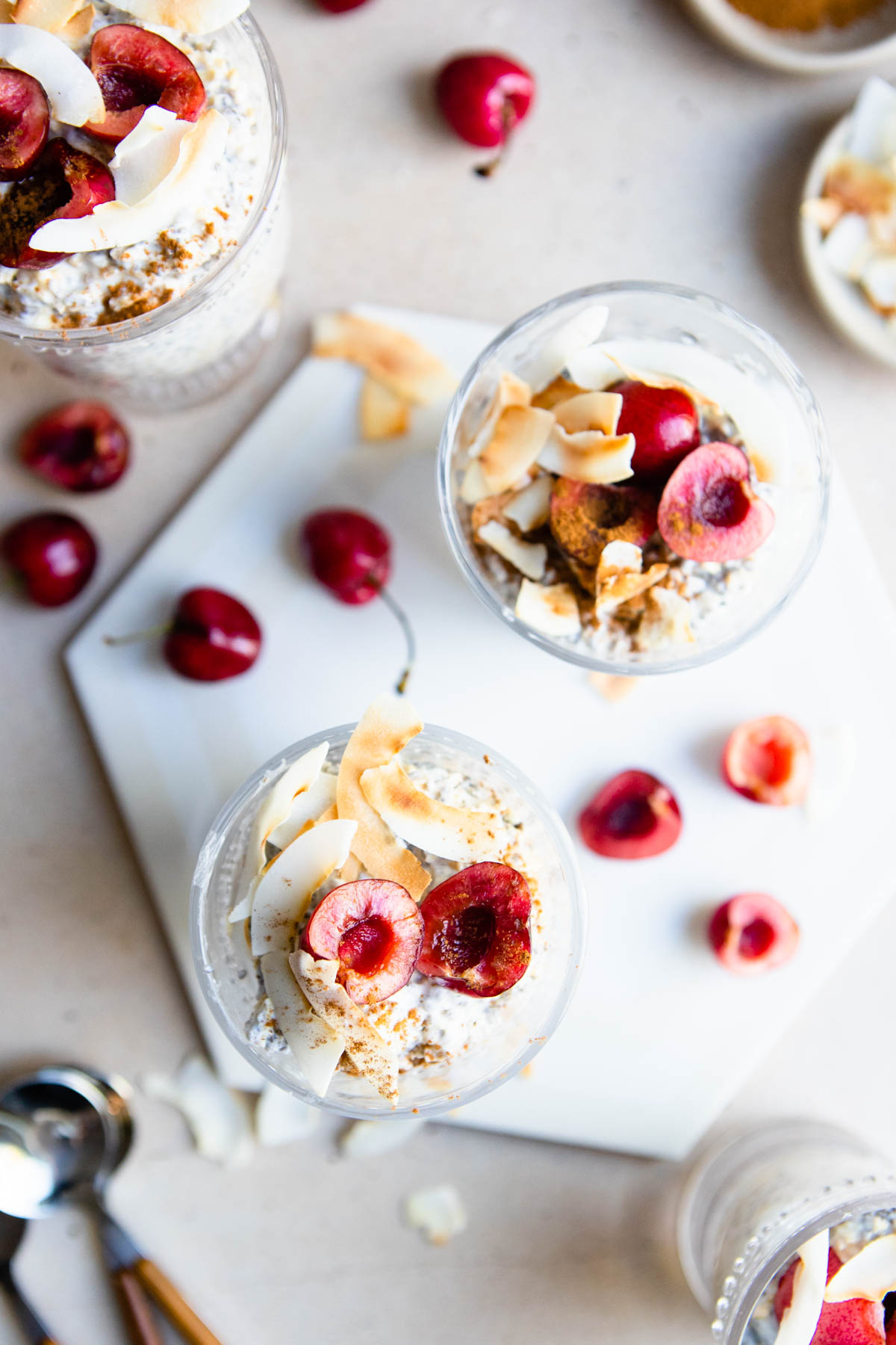 4 glass cups filled with overnight oats made with kefir and chia seeds, and topped with cherries and toasted coconut flakes 