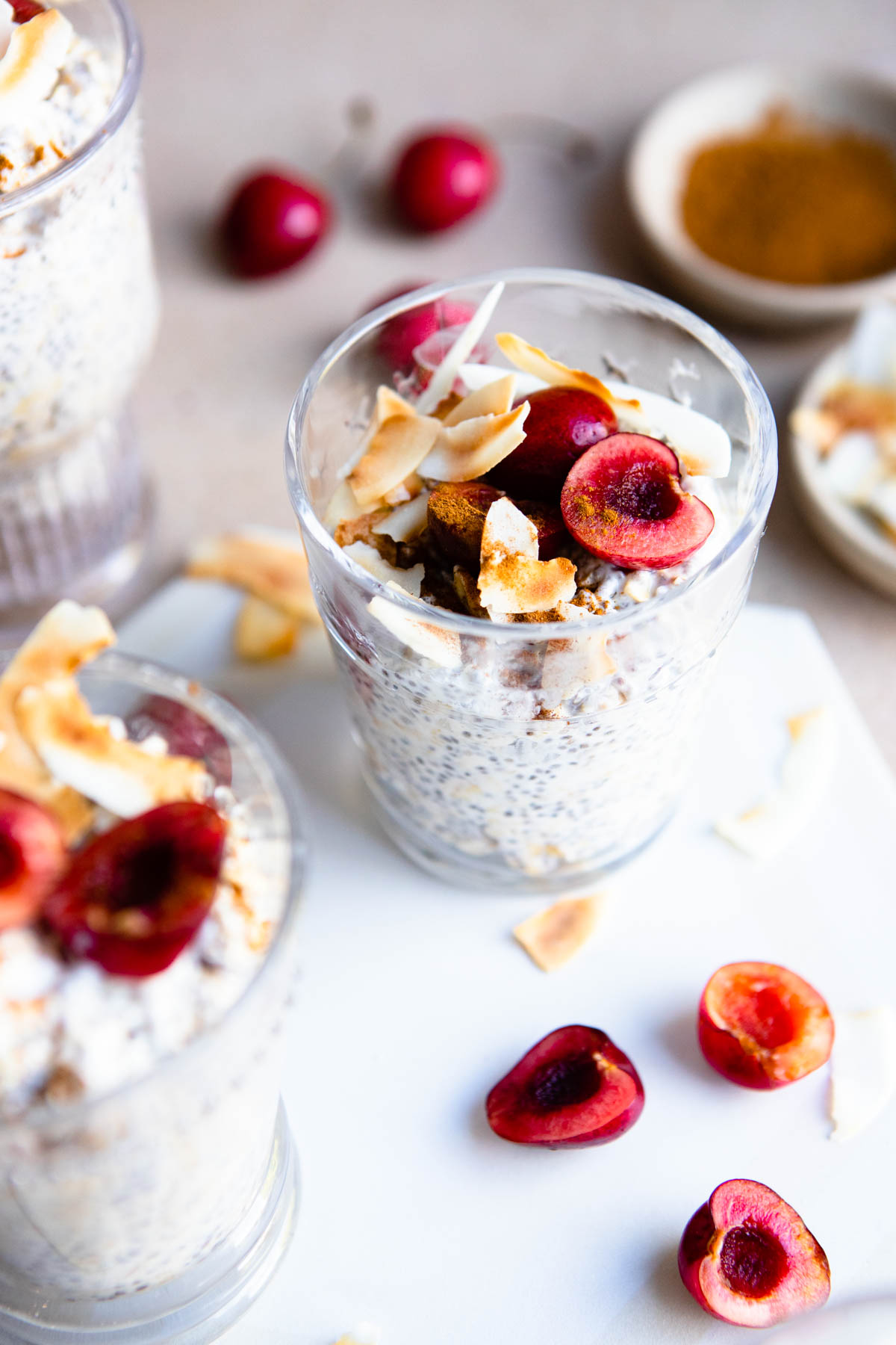 3 glasses filled with kefir overnight oats and topped with coconut flakes and cherries 
