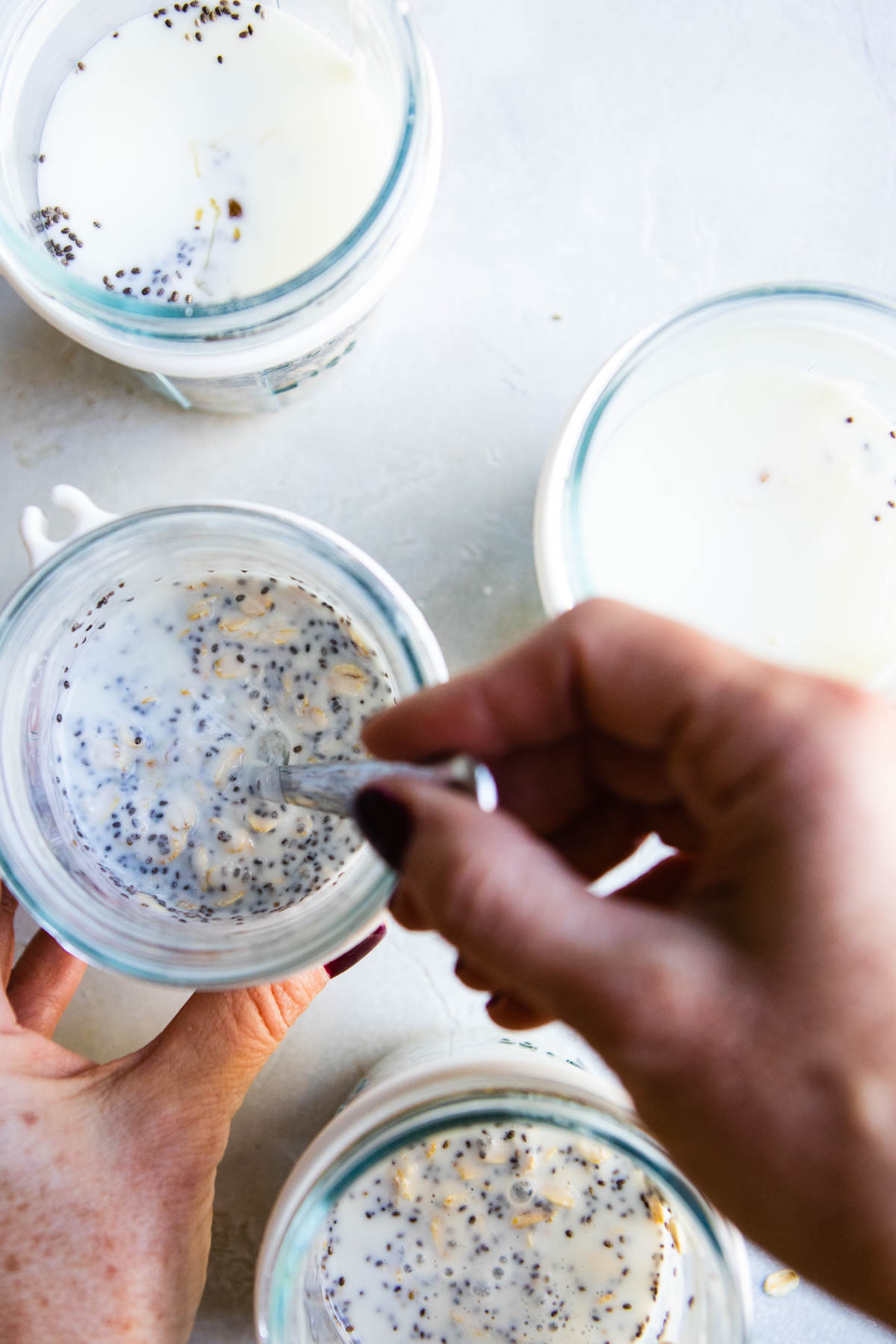 overnight oats being stirred in glass mason jars