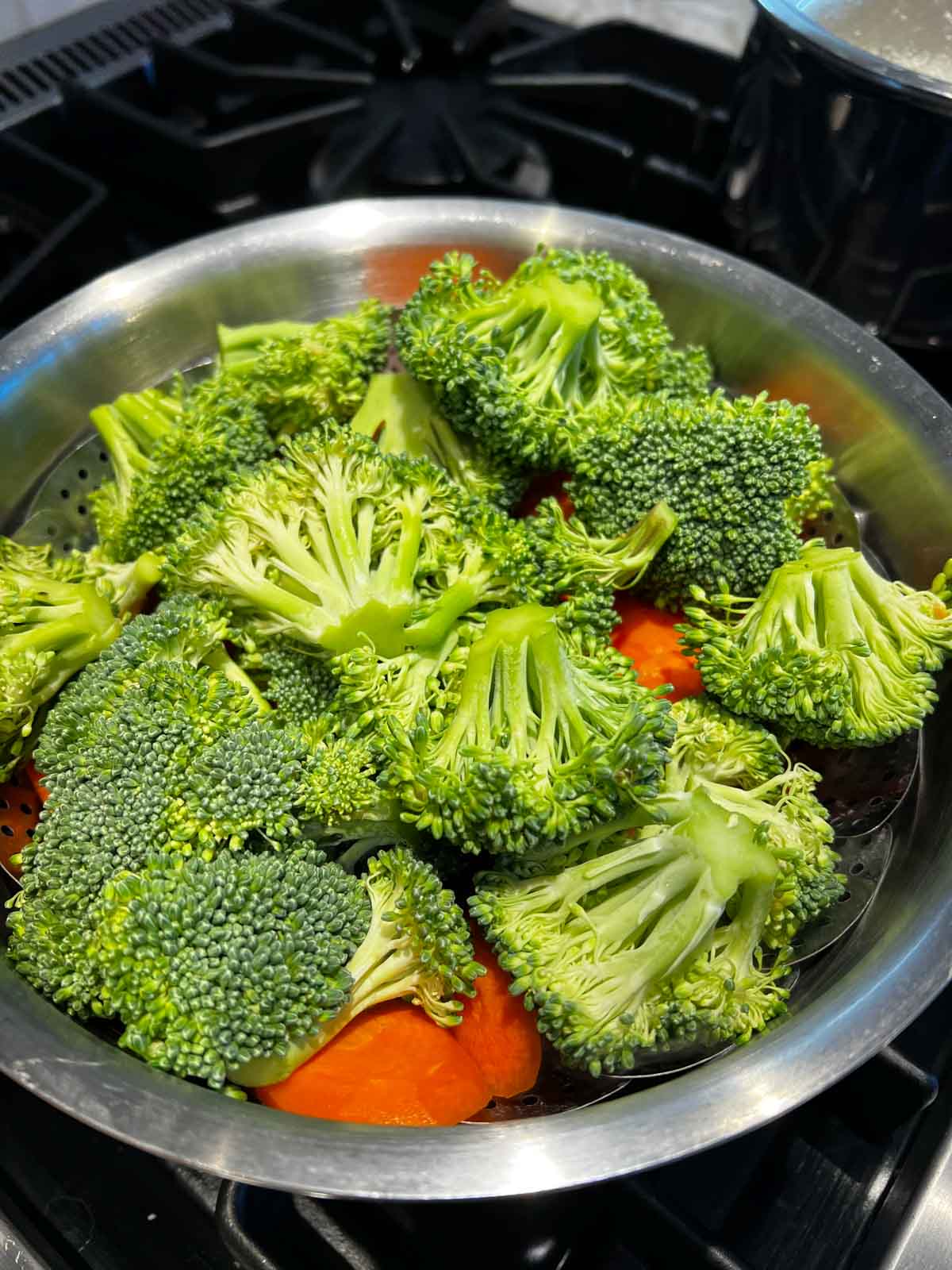raw broccoli and carrots in a steamer basket on the stove top