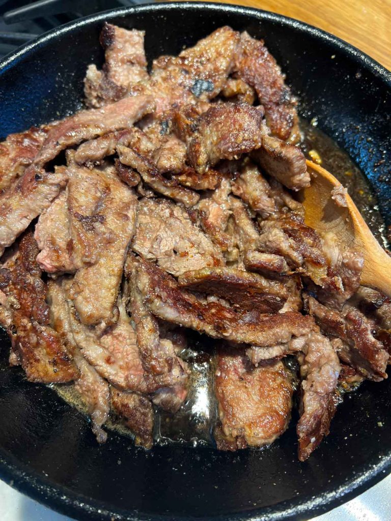 cooked flank steak added to a pan with teriyaki sauce to make beef teriyaki