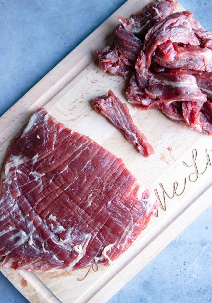 a large piece of flank steak cut in half on a cutting board