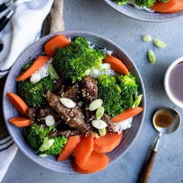teriyaki beef served over a bed of rice with steamed carrots and broccoli in a round gray bowl