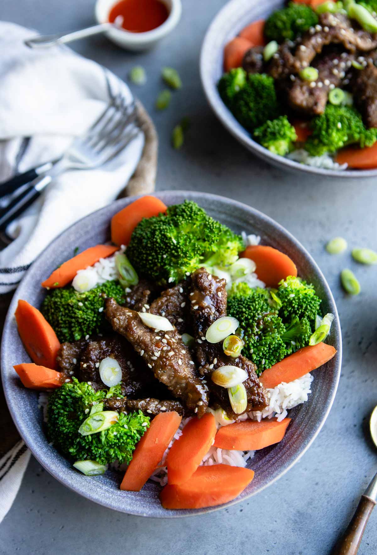 2 beef teriyaki bowls filled with white rice and steamed vegetables in gray bowls
