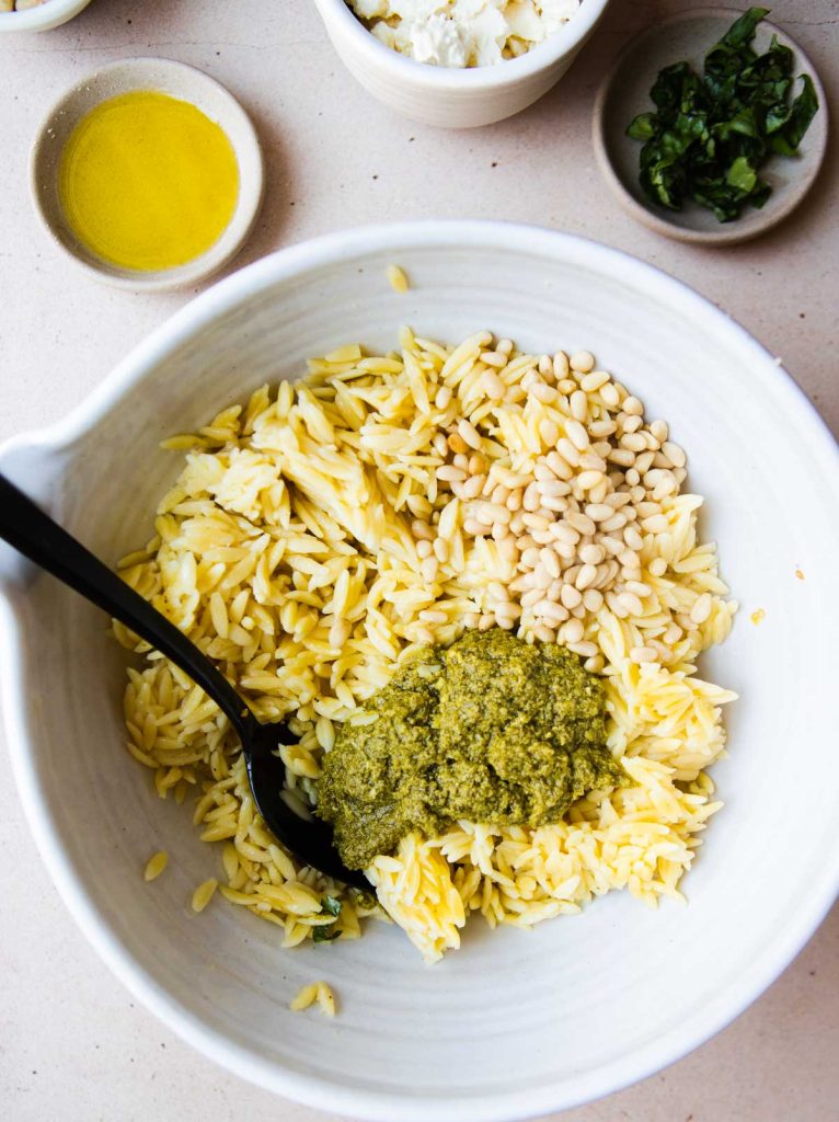 cooked orzo being tossed with pine nuts, olive oil and pesto 