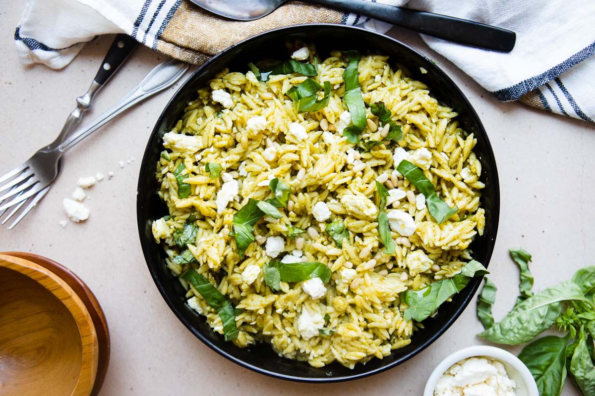 black bowl filled with orzo pesto salad topped with feta cheese 