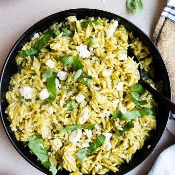 chilled orzo salad in a black dish garnished with fresh basil and feta cheese
