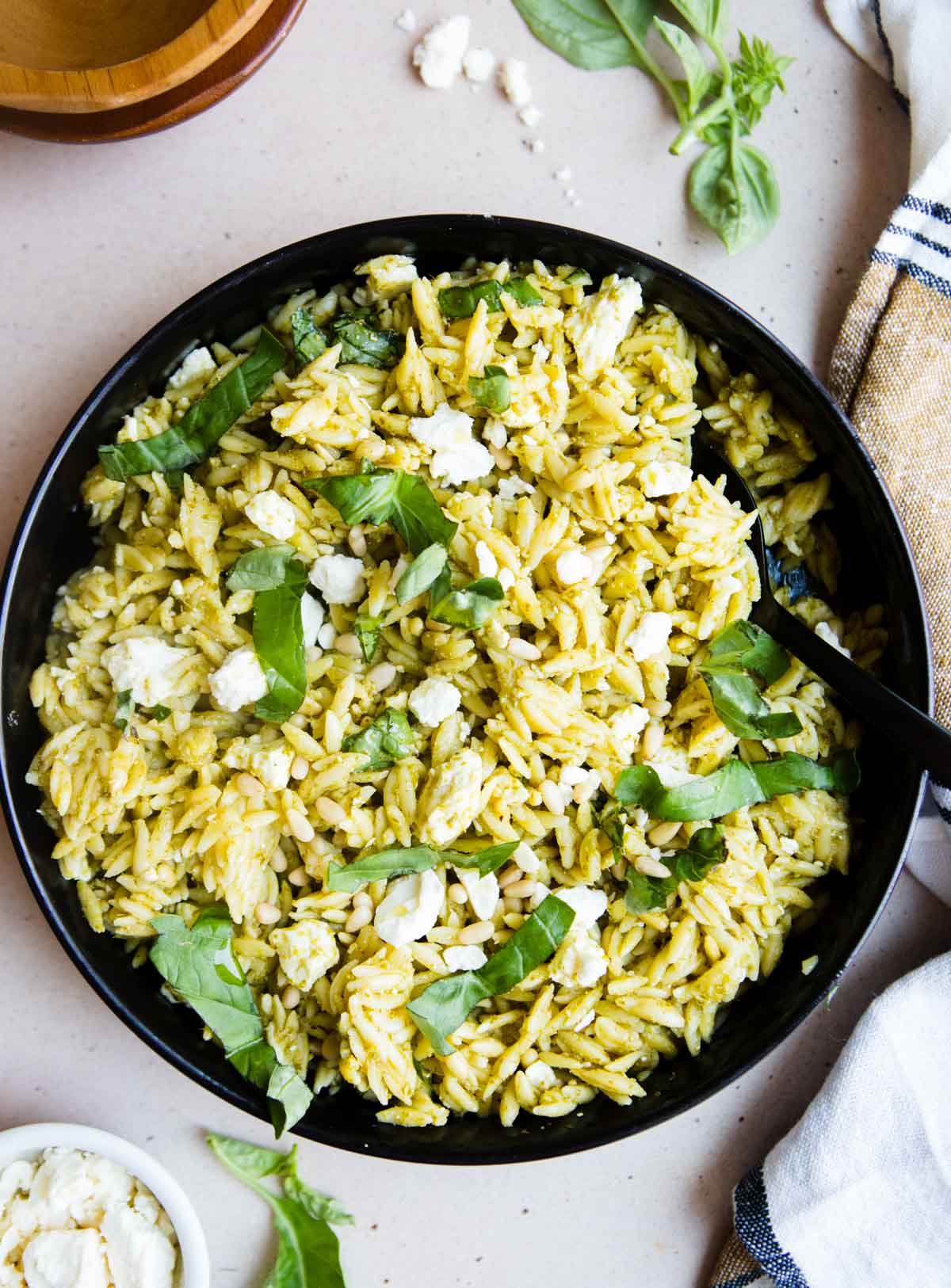 chilled orzo salad in a black dish garnished with fresh basil and feta cheese