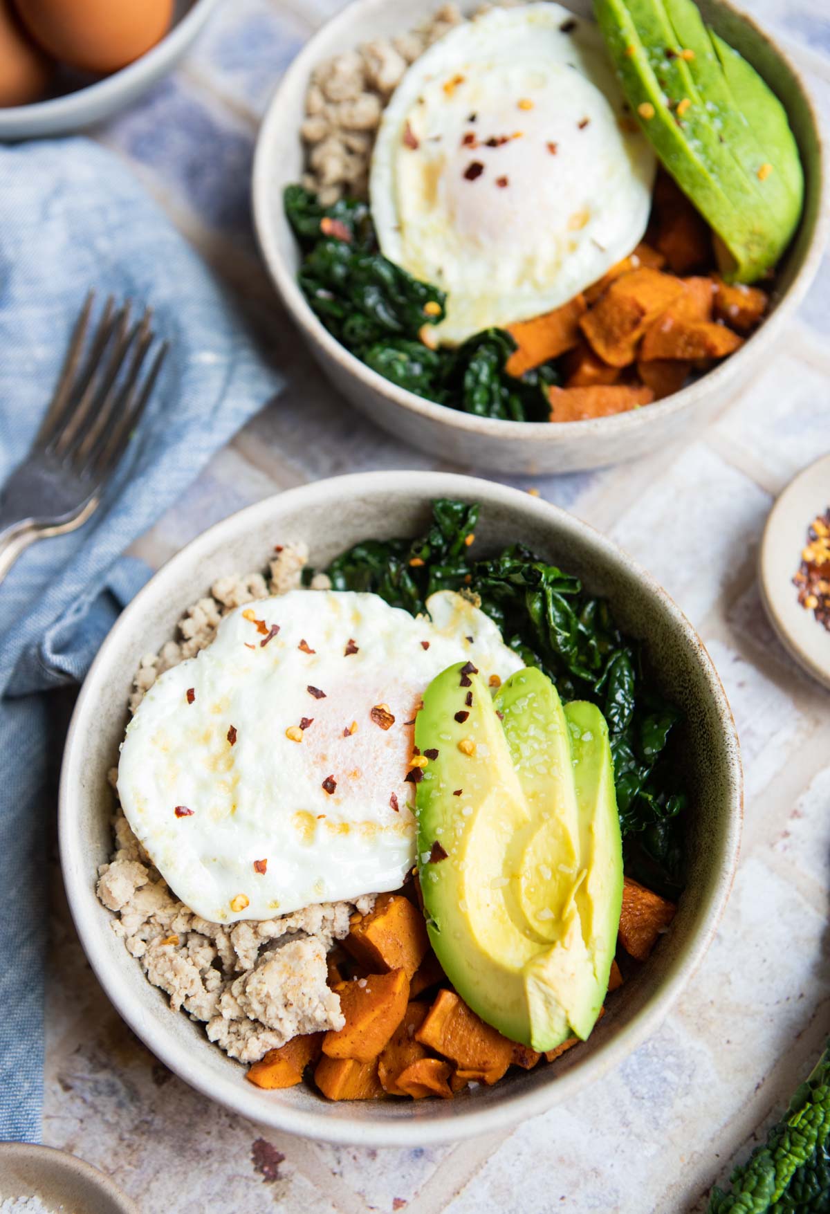 beige bowls filled with cooked kale, ground turkey, sweet potatoes and topped with an egg and avocado 