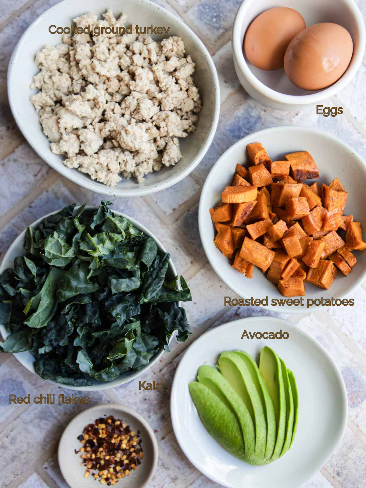 cooked ground turkey, raw kale, eggs, avocado and cooked sweet potatoes on white plates 