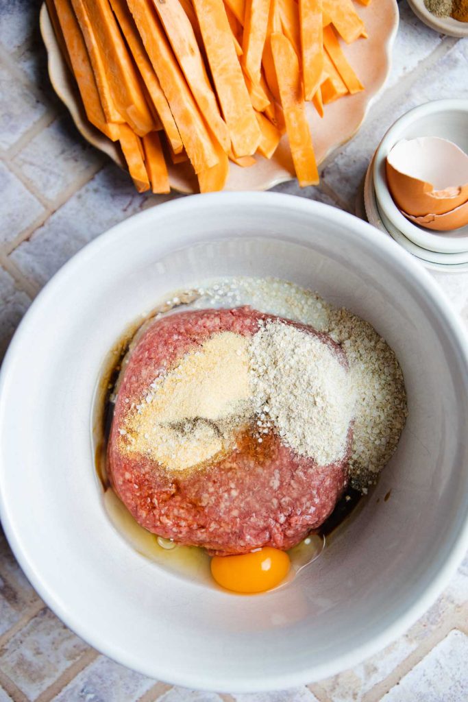 ground beef in a bowl with egg, milk, seasonings and breadcrumbs ready to make hamburgers