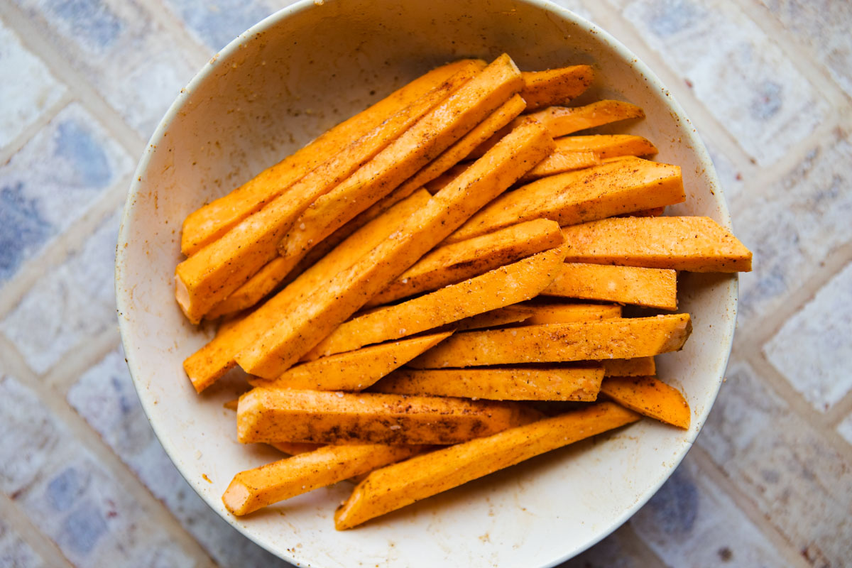 raw sweet potato wedges on a bowl tossed with herbs and spices