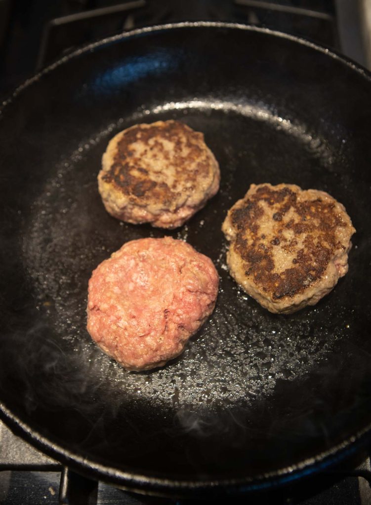 juicy burger patties being grilled in a cast iron skillet