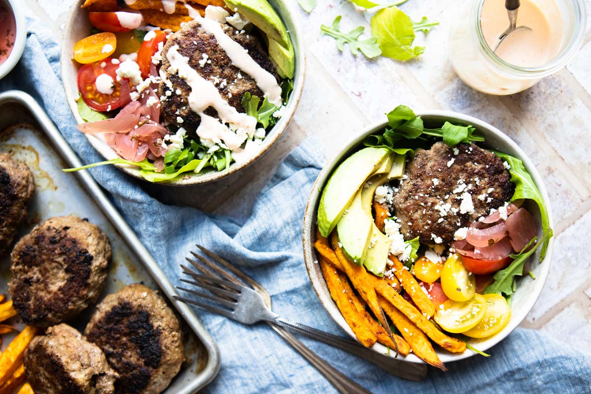 2 round bowls filled with salad, hamburger patty and toppings for a burger salad