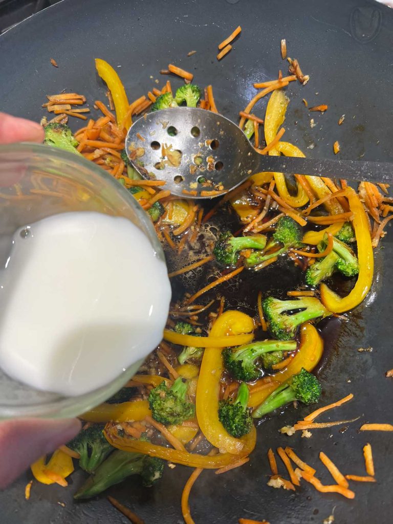a slurry of cornstarch and water being added to a wok with veggies and teriyaki sauce