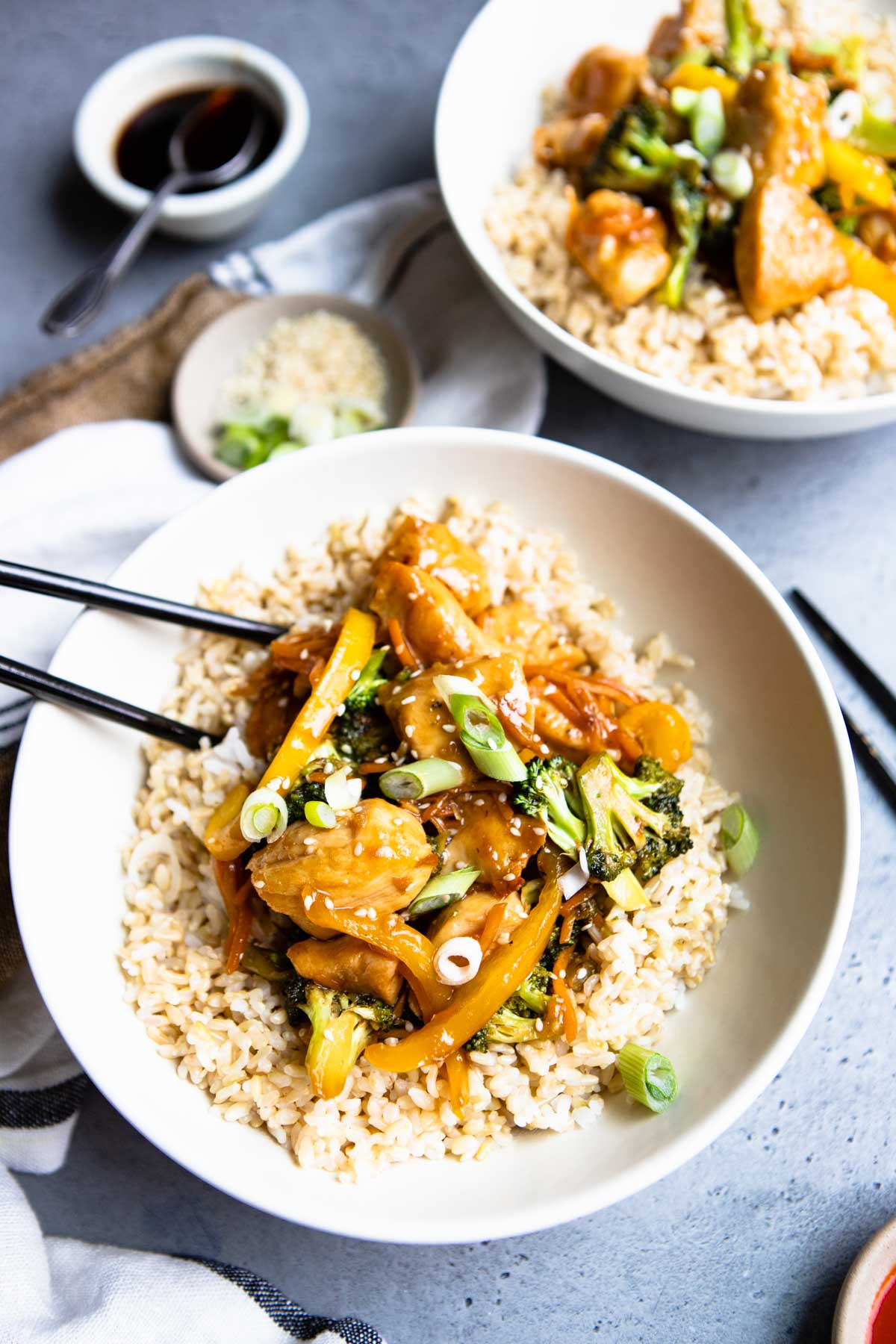 brown rice, vegetables and chicken teriyaki in a white bowl with black chopsticks
