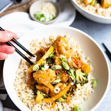 a white bowl filled with brown rice and chicken teriyaki and vegetables