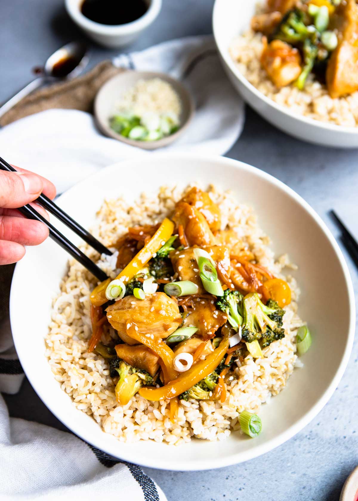 a white bowl filled with brown rice and chicken teriyaki and vegetables 