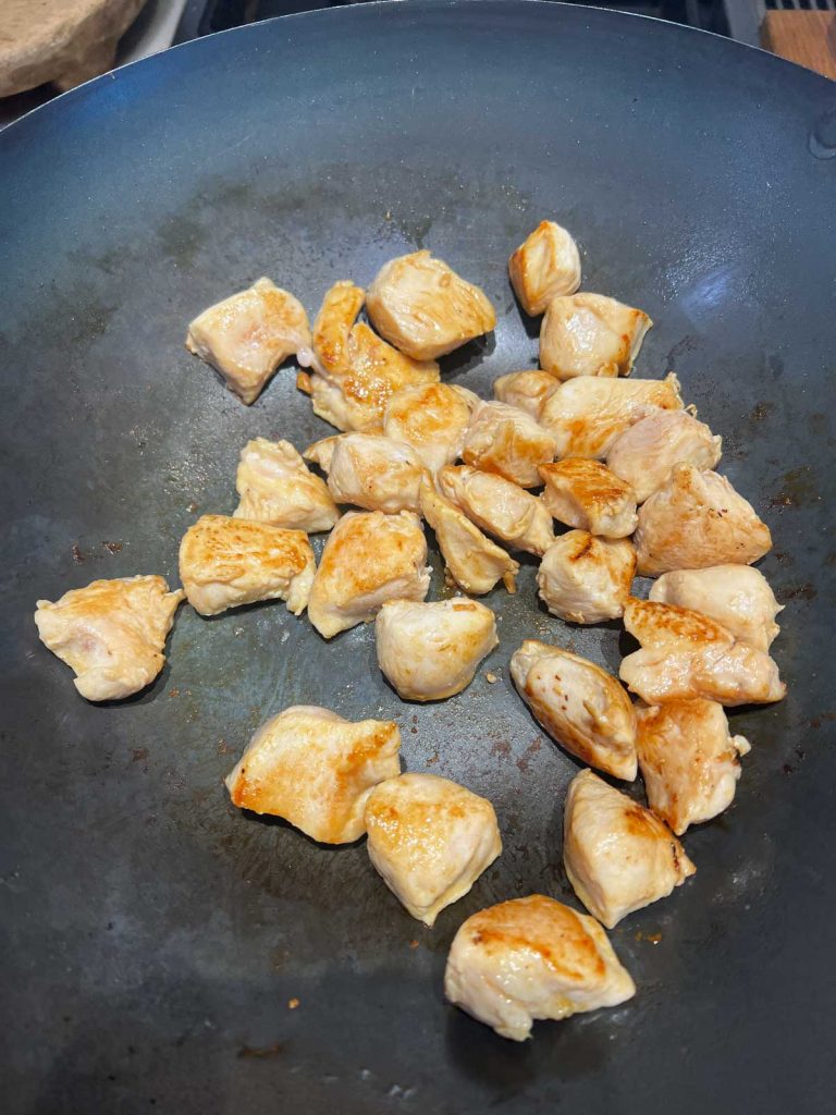 chicken breast chunks being cooked in a wok