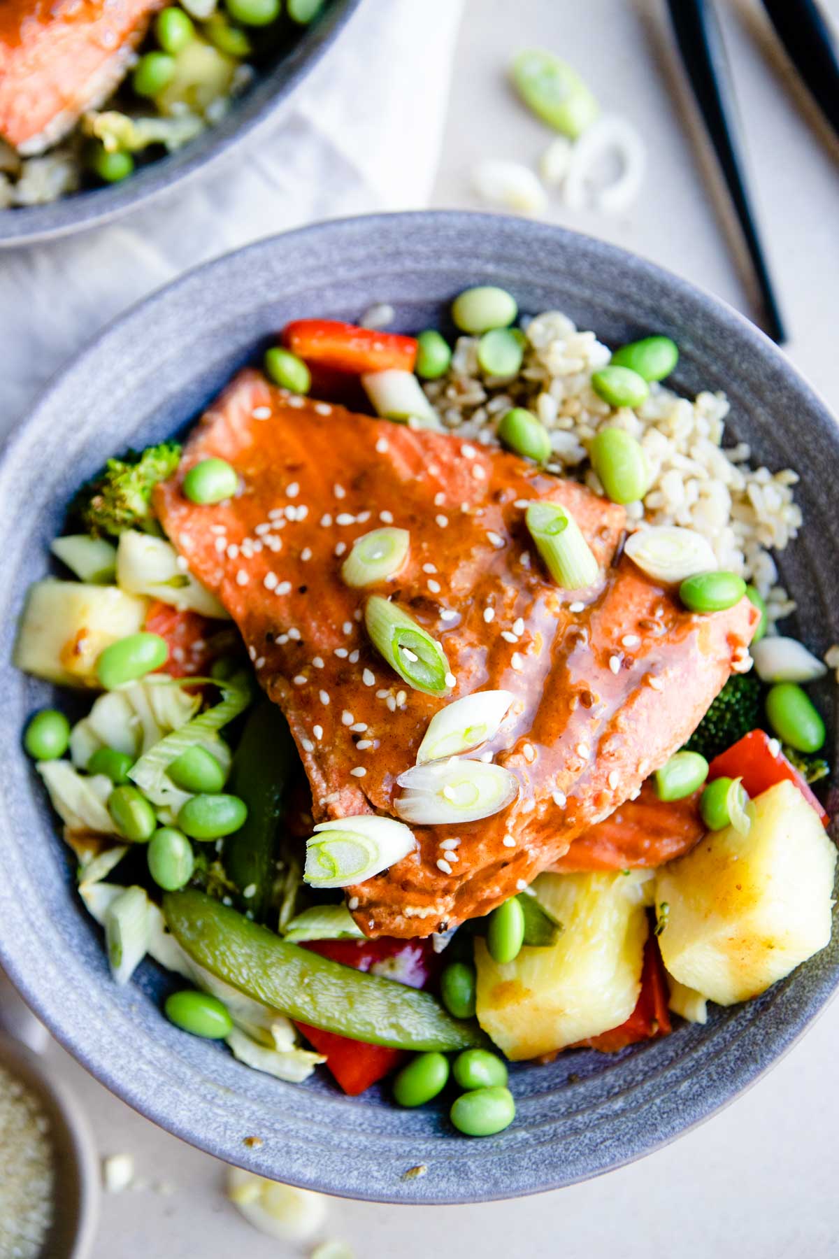 a gray bowl with rice, vegetables, pineapple and salmon teriyaki