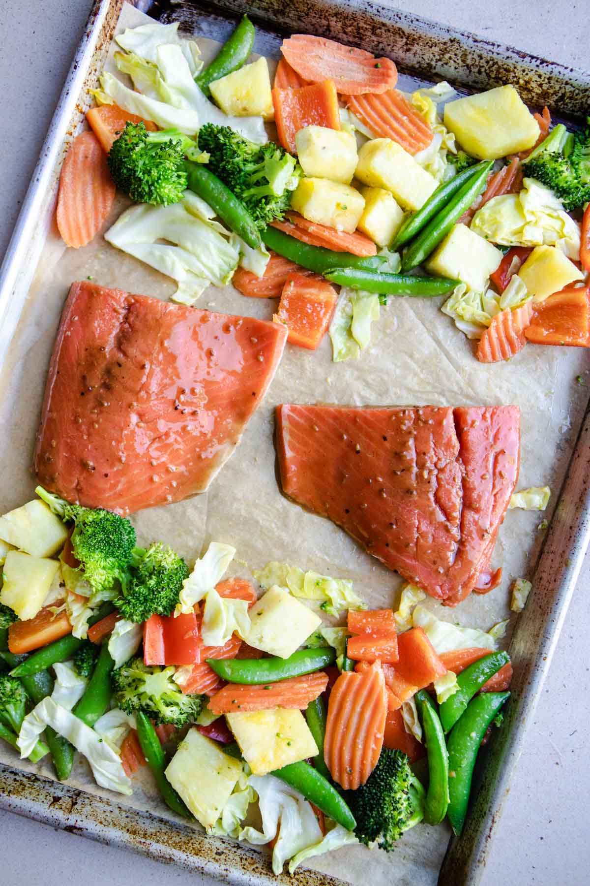 raw salmon teriyaki placed on a sheet pan with vegetables and pineapple, and ready to go in the oven to cook