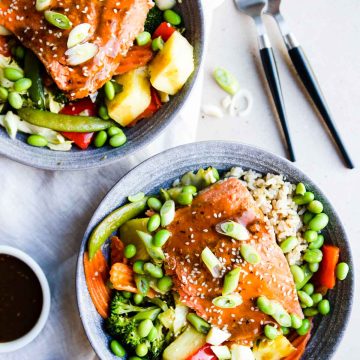 2 gray bowls filled with rice, vegetables, pineapple and salmon teriyaki