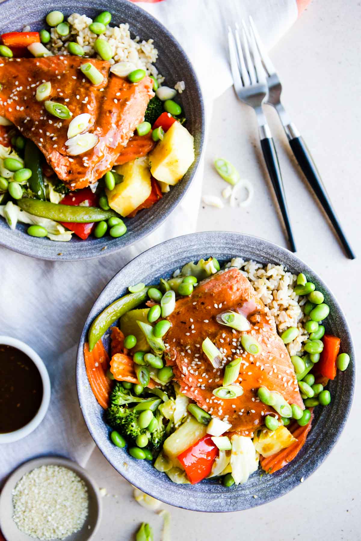 2 gray bowls filled with rice, vegetables, pineapple and salmon teriyaki 