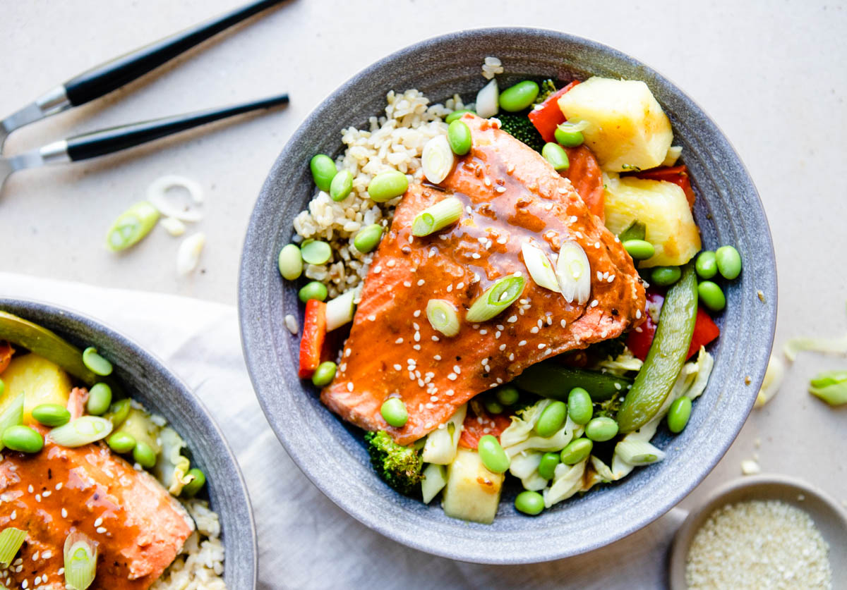 a salmon filet glazed with teriyaki sauce and placed on a bowl of vegetables and pineapple and rice