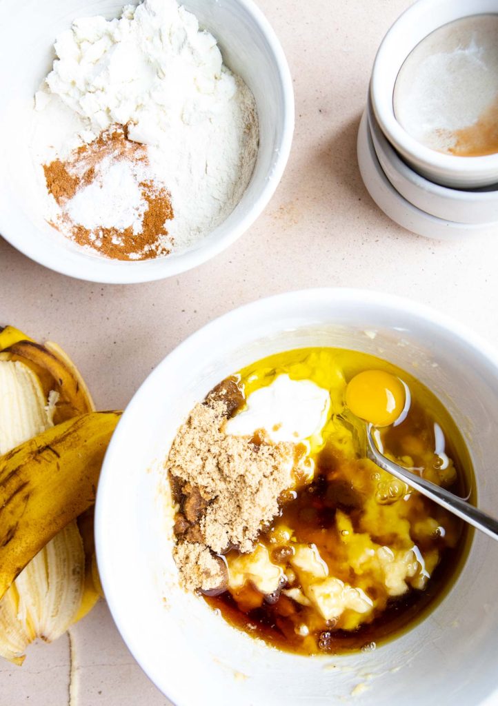mashed bananas with the "wet ingredients" mixed in a white bowl, ready to make banana protein muffins 