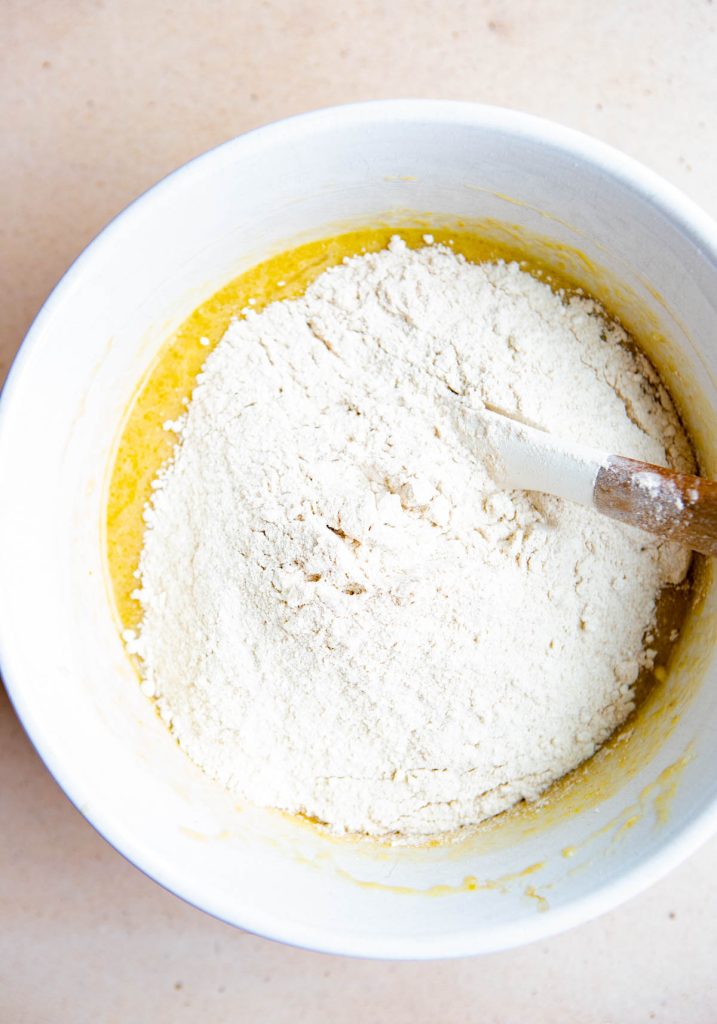 flour added to banana bread mix in a large white mixing bowl