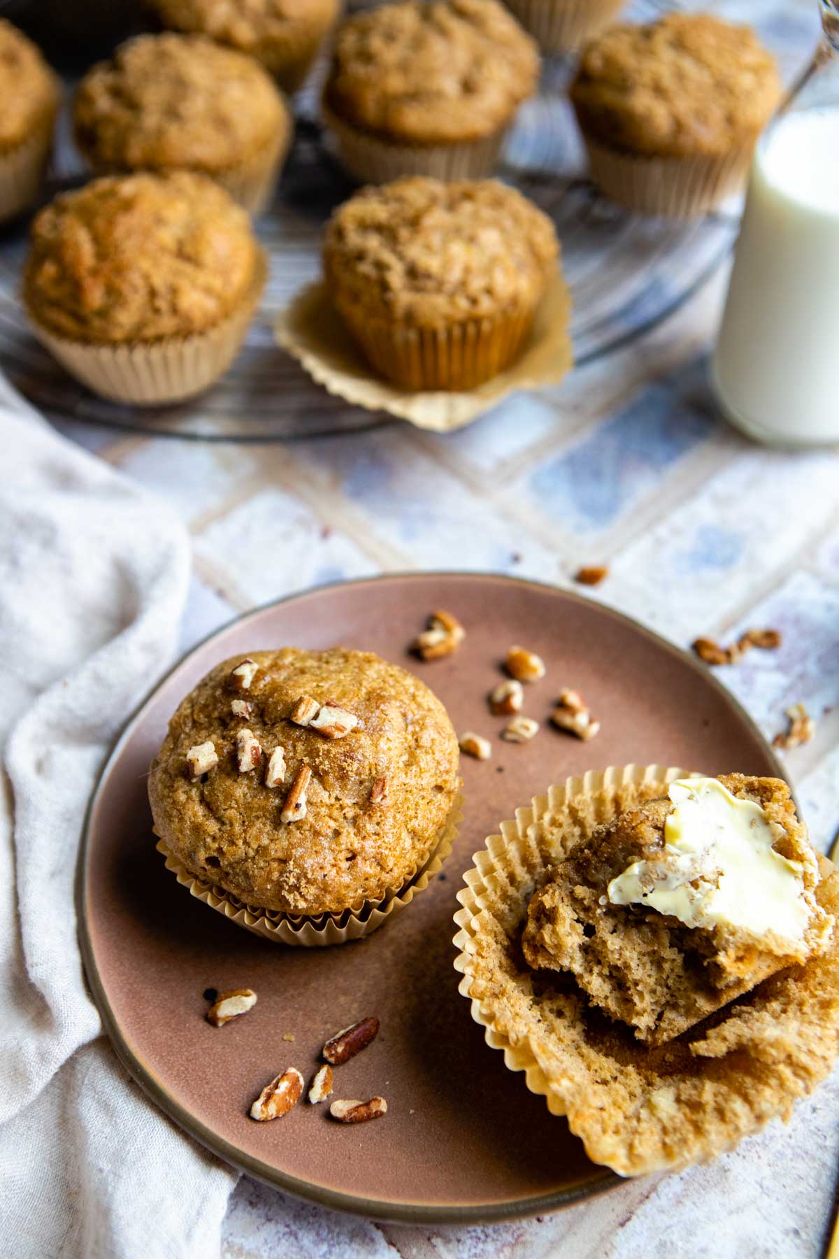 a small brown plate with 2 banana protein muffins on top, one of them spread with soft butter