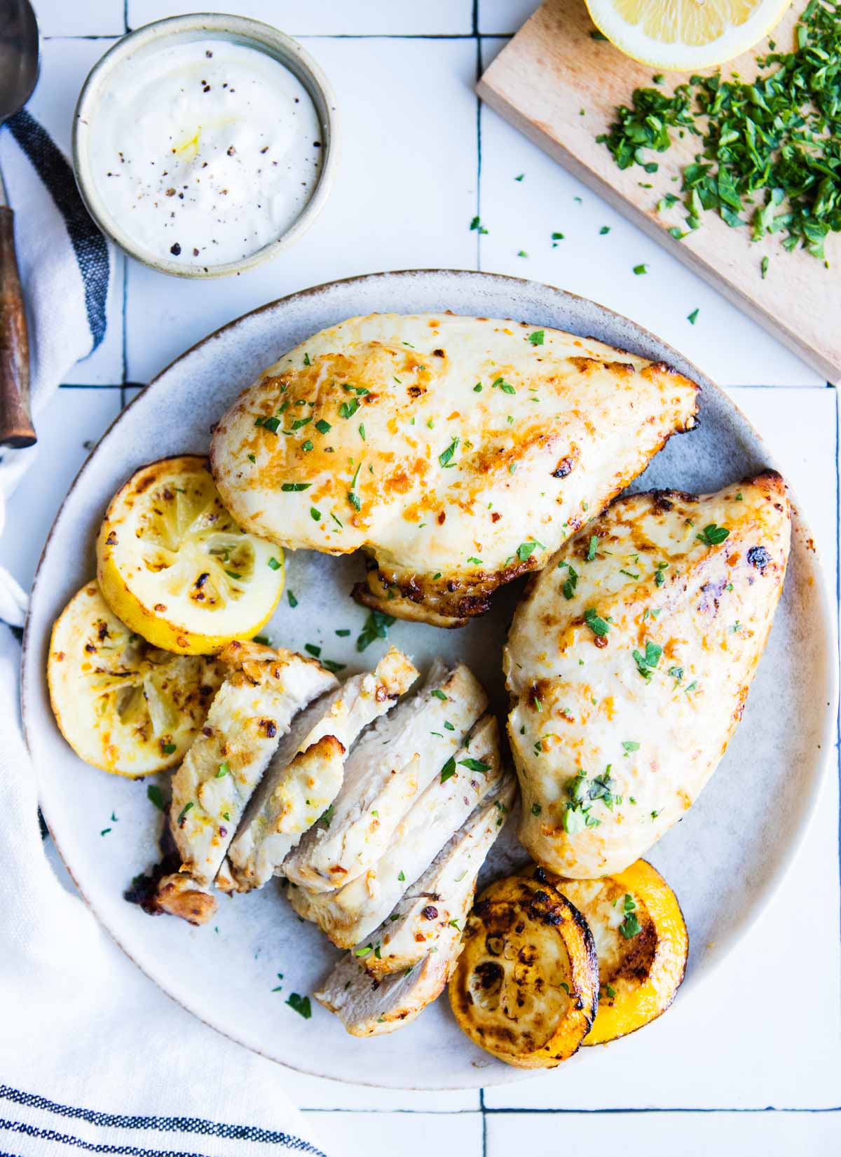 whole and sliced air fryer lemon chicken breasts on a gray plate garnished with grilled lemons
