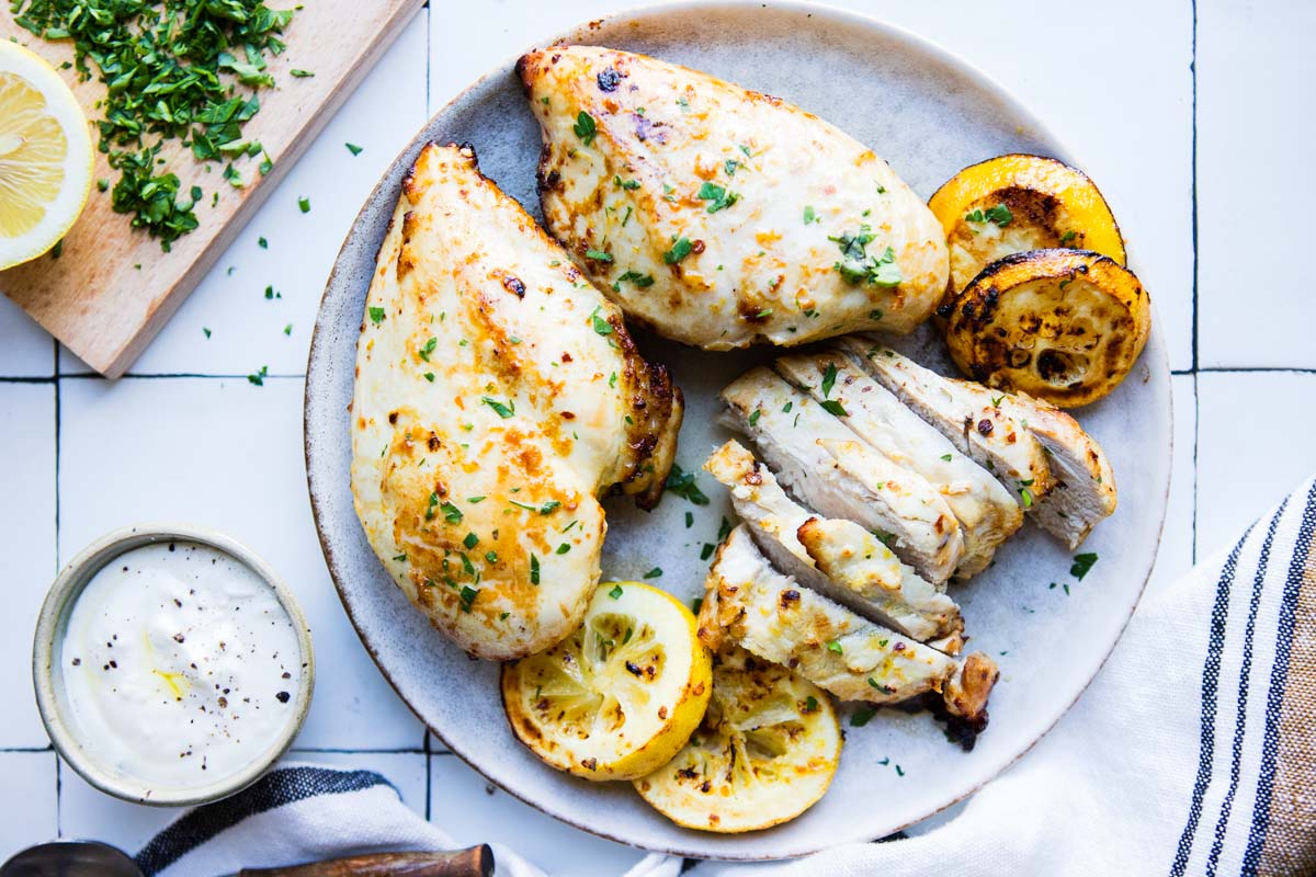 a gray plate filled with lemon herbed chicken breasts cooked in the air fryer and garnished with grilled lemons