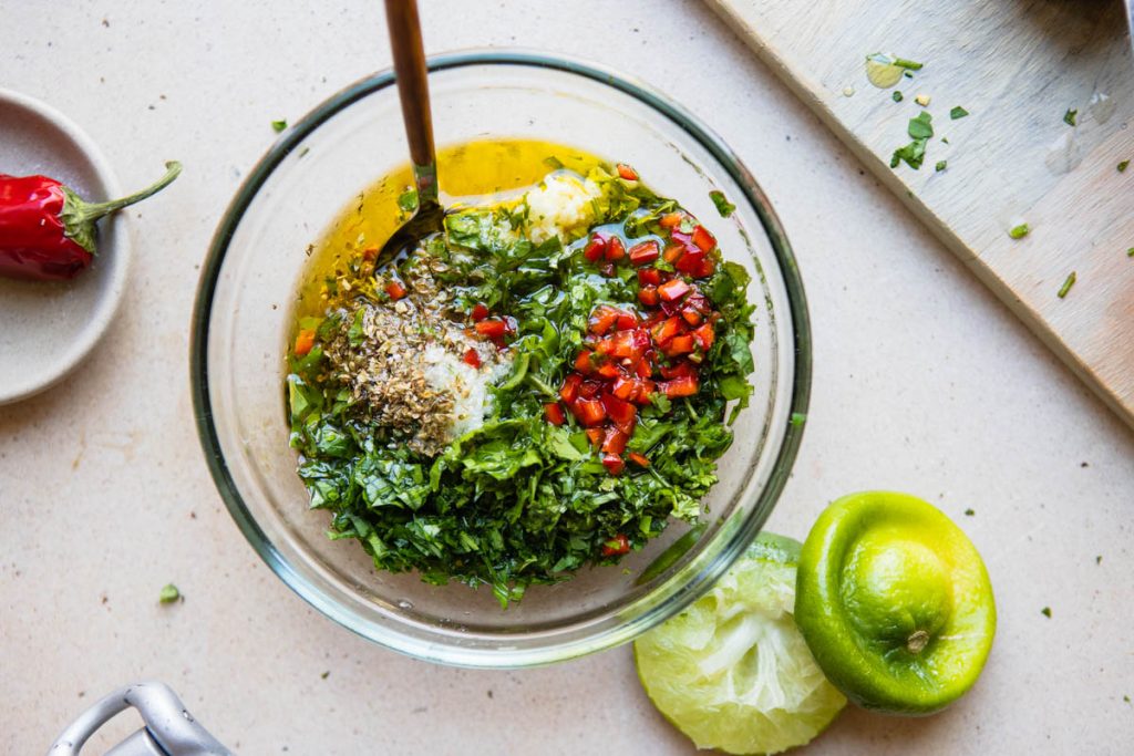 olive oil and lemon juice added to a bowl of herbs to make cilantro chimichurri sauce