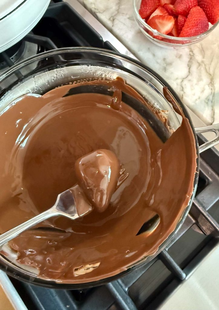 strawberries being dipped in melted chocolate 