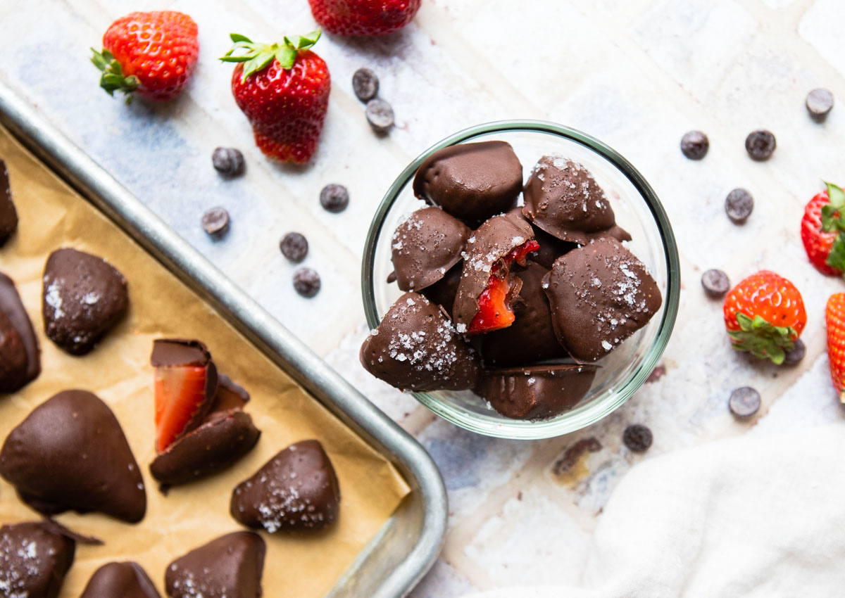 chocolate covered frozen strawberries in a glass bowl and on a parchment lined baking tray