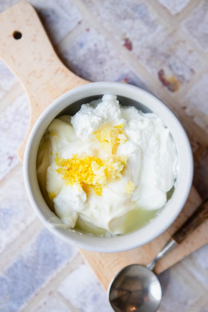 ingredients to make yogurt sauce for chicken in a white bowl set on a wooden board 