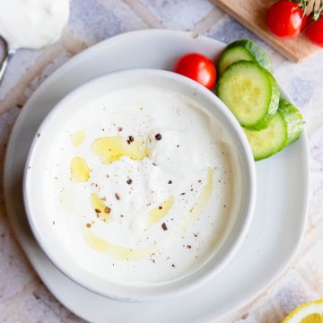 garlic yogurt sauce in a white ceramic bowl with sliced cucumbers and cherry tomatoes