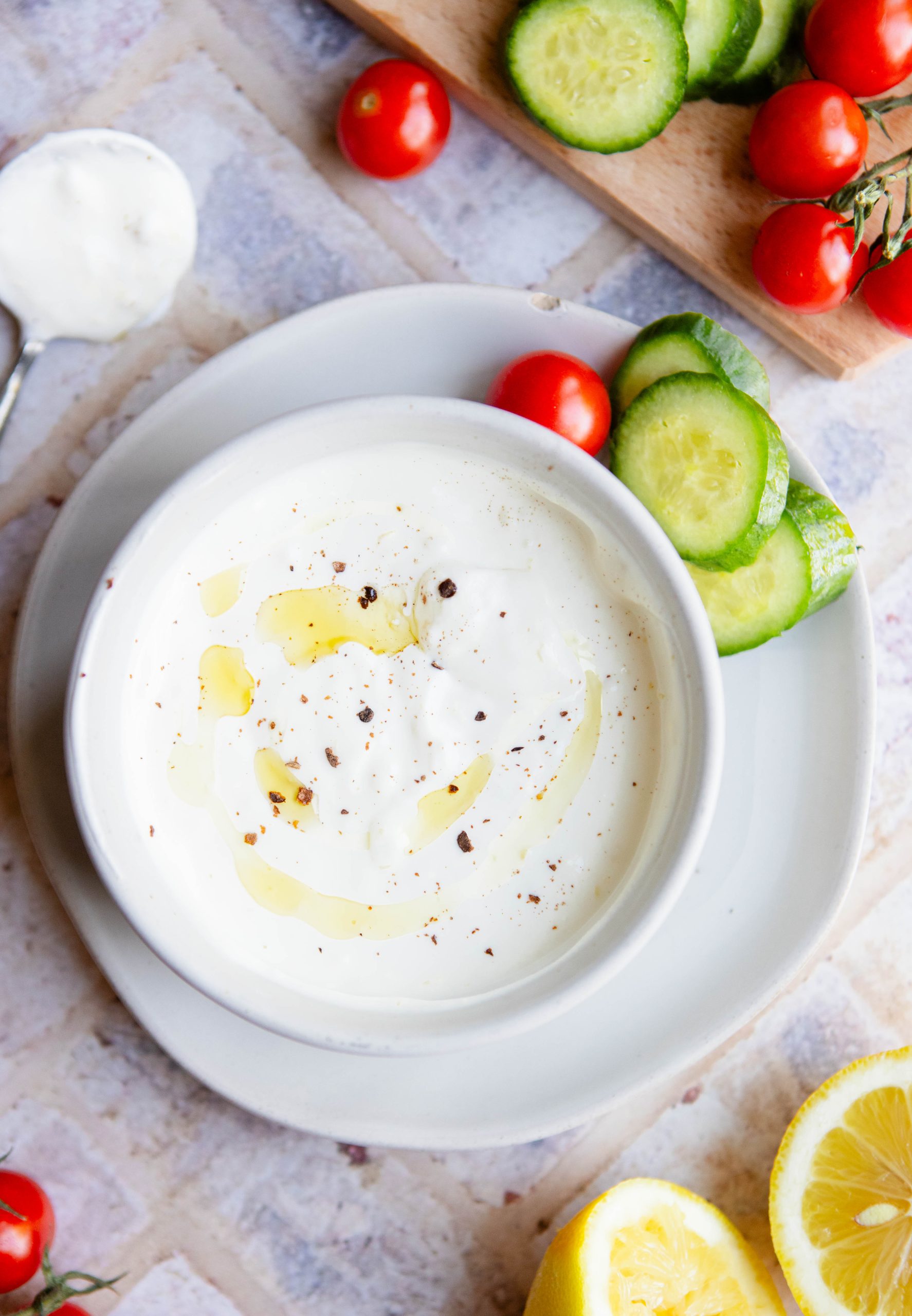 garlic yogurt sauce in a white ceramic bowl with sliced cucumbers and cherry tomatoes
