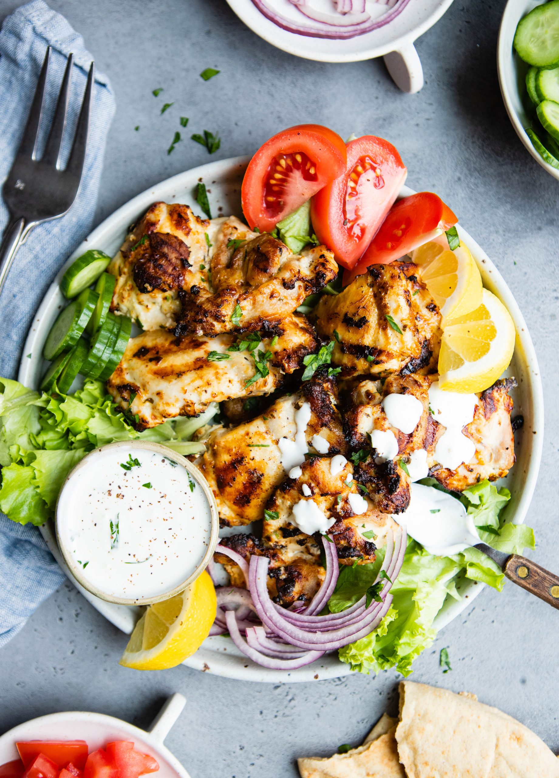 a plate filled with grilled chicken thighs and a bowl of garlic yogurt sauce