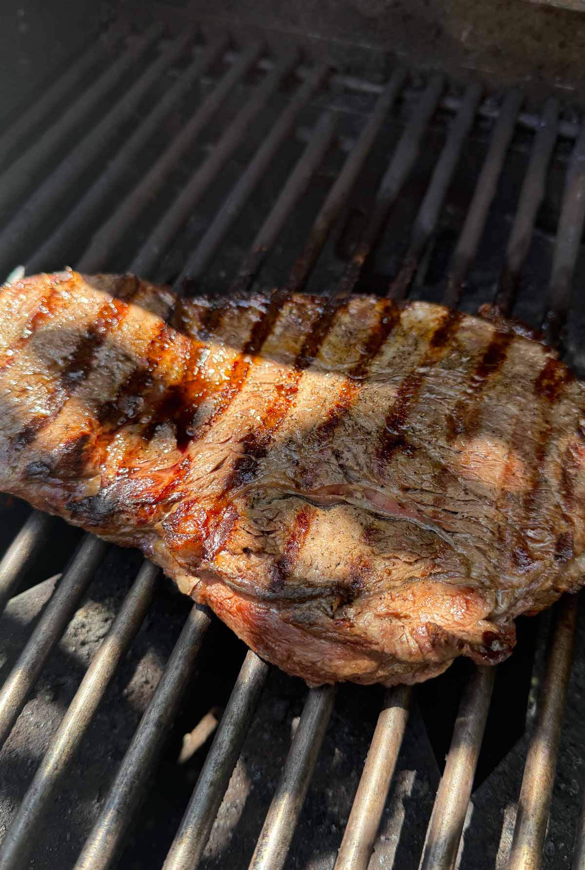top sirloin steak grilling on an outdoor gas grill